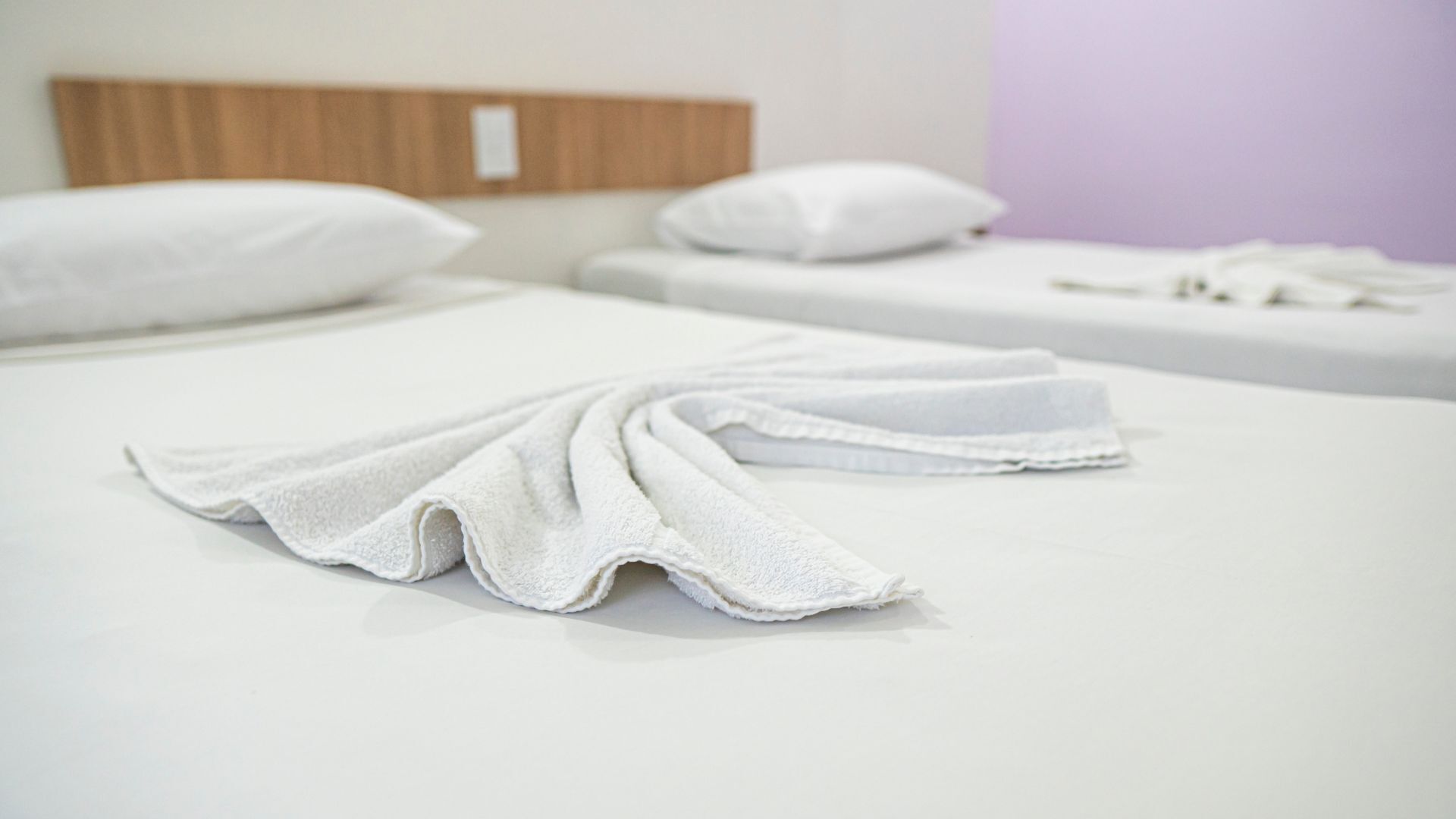 Quarto de hotel com duas camas, roupa de cama branca e cabeceira de madeira.