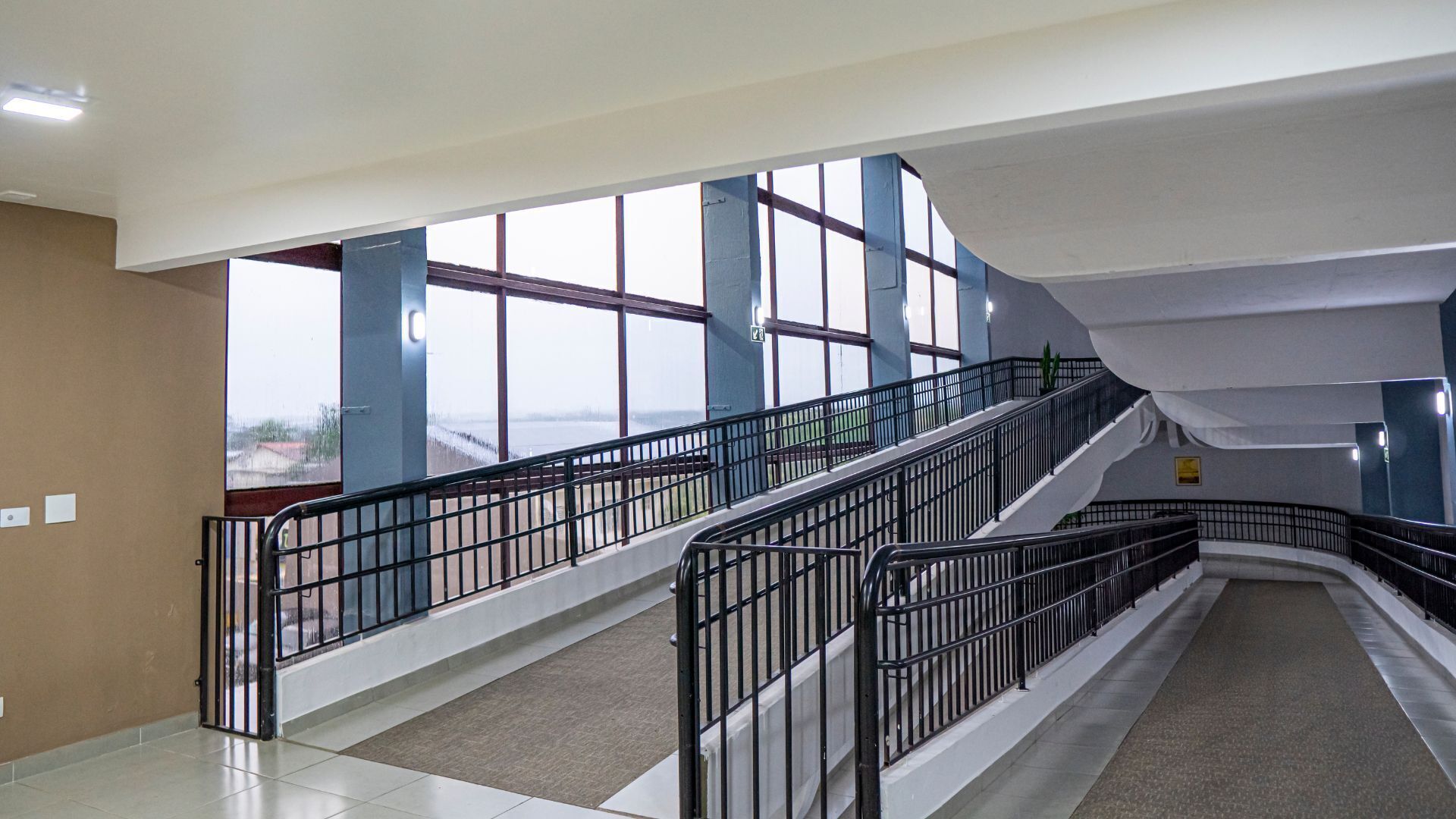 Un intérieur à plusieurs niveaux, doté d’un escalier, de rampes en métal et de grandes fenêtres offrant une vue dégagée.