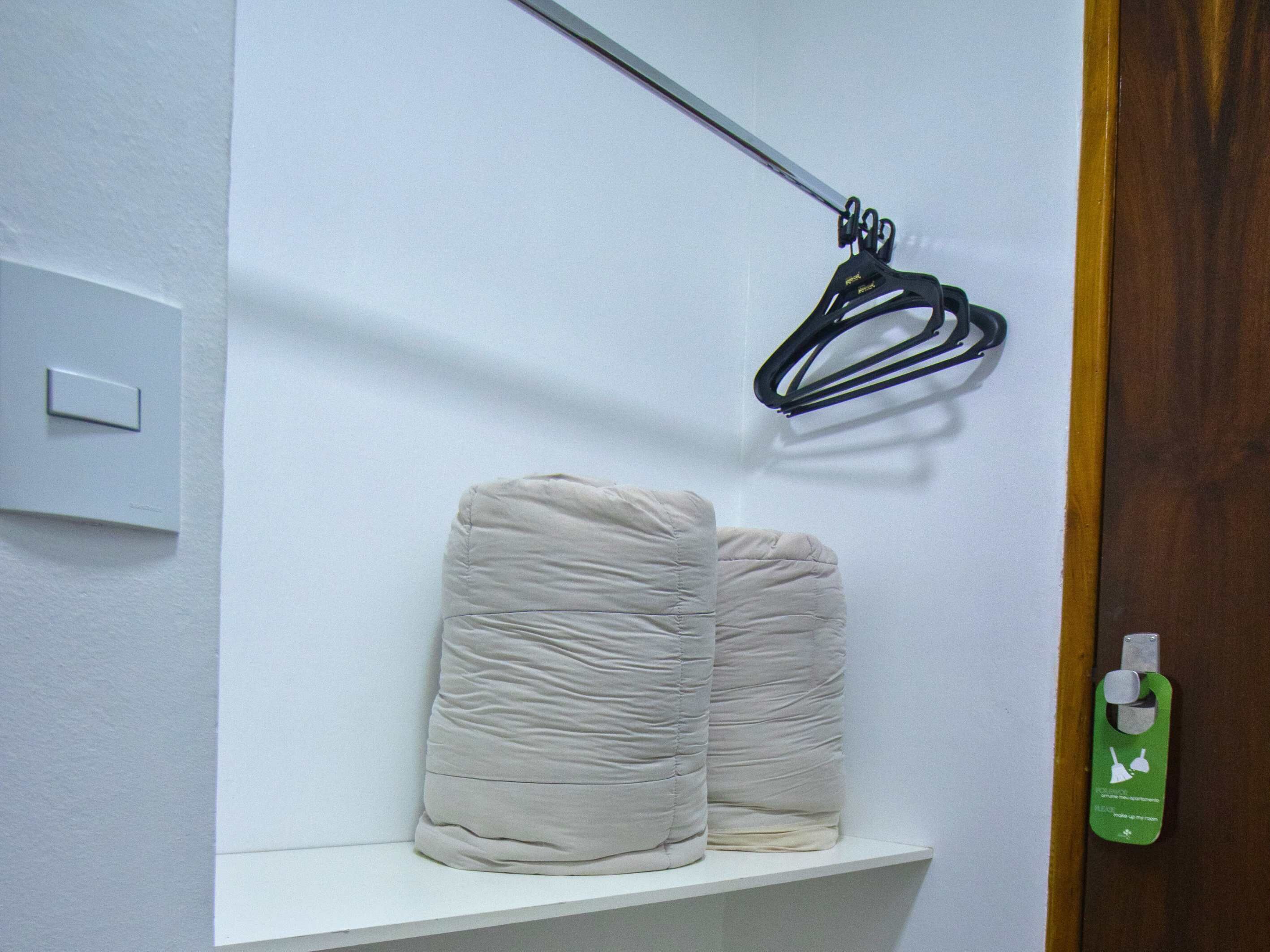 A bathroom with a white shelf holding two rolled-up towels, a black hanger, and a green bottle with a label.