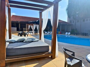 A bed with a canopy, a pool, and outdoor seating. - Manacá Hotel (Foz do Iguaçu)