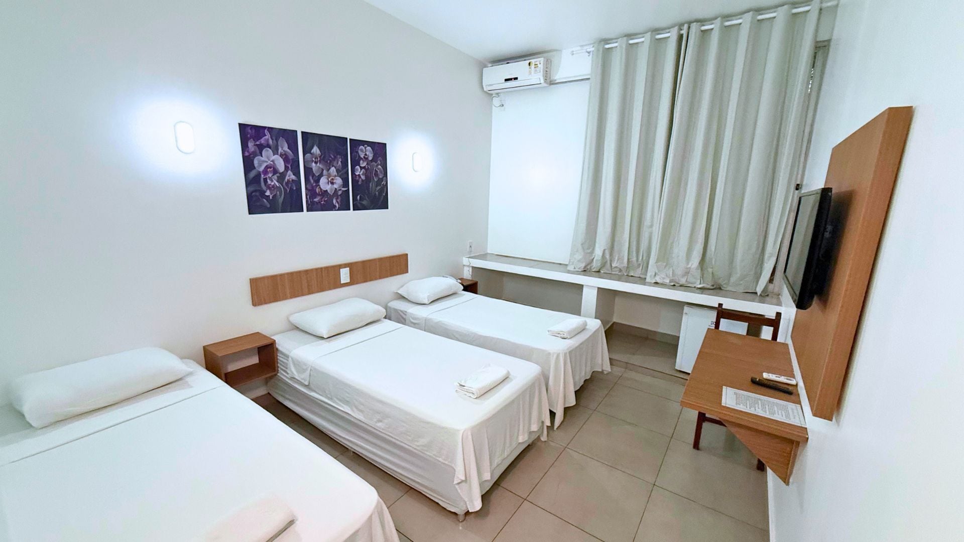 A hotel room with two single beds, a desk, a chair, a TV, and a window with curtains.