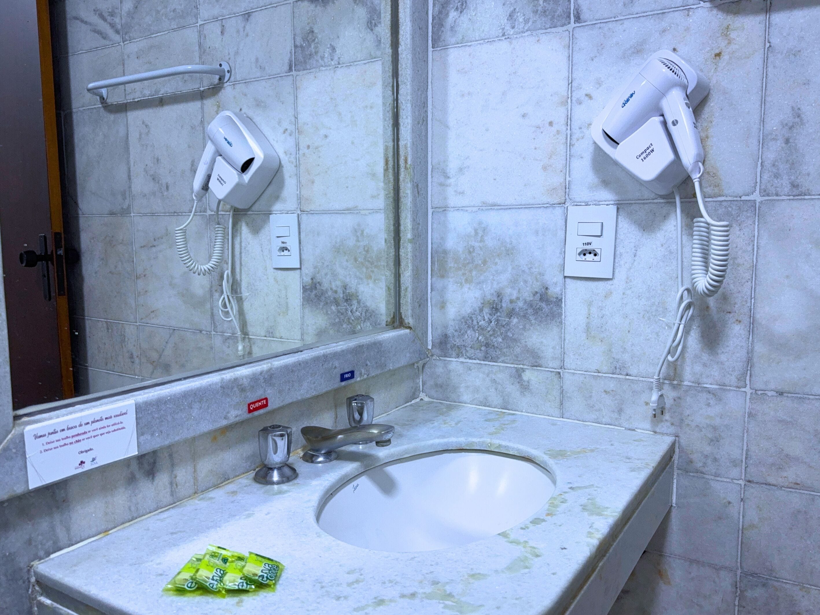 Un baño con un lavamanos, dos secadores de pelo montados en la pared y un espejo sobre el lavamanos.