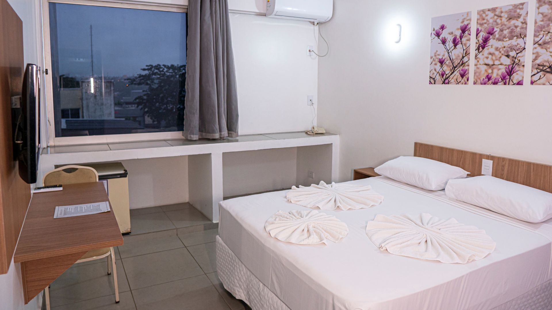 Habitación de hotel con cama, escritorio, silla, ventana y aire acondicionado de pared.