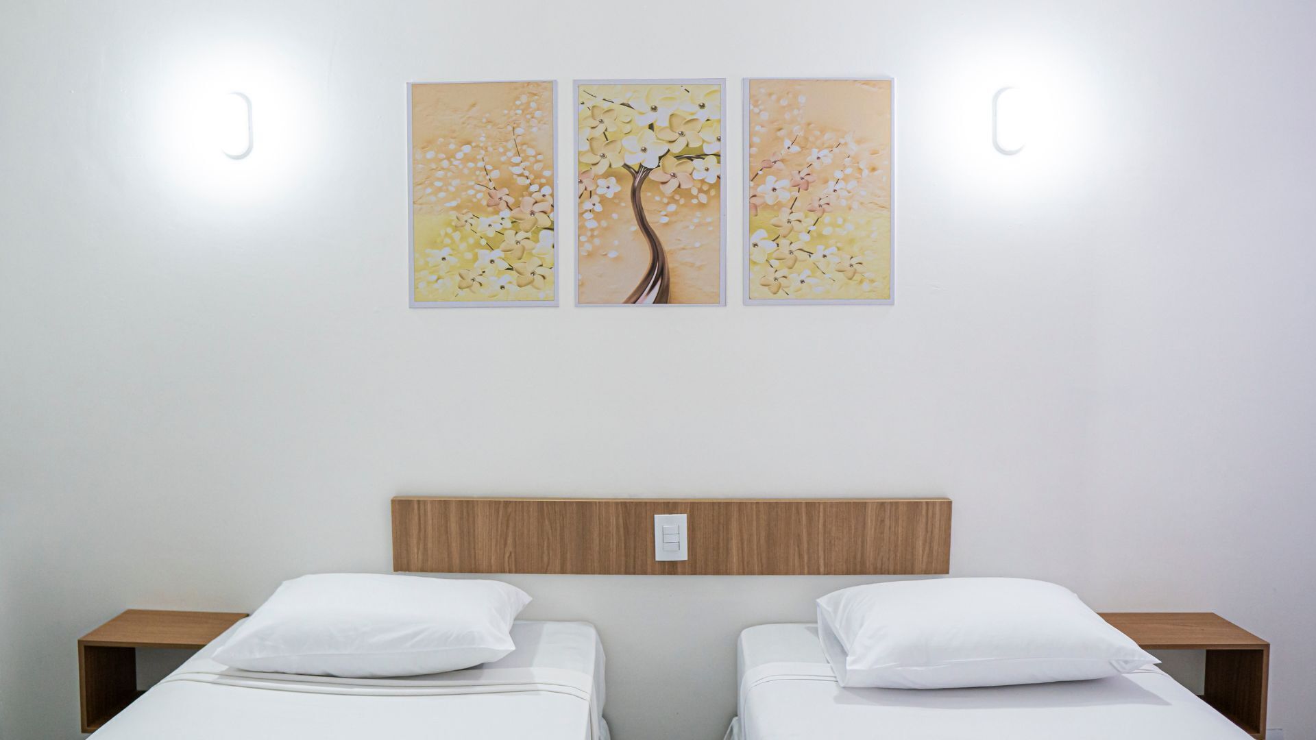 Ein Hotelzimmer mit zwei Einzelbetten, einem hölzernen Kopfteil und drei an der Wand befestigten Bildern.