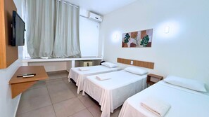 Habitació d'hotel amb dos llits individuals, una televisió, una finestra amb cortines i un aire condicionat fixat a la paret.
