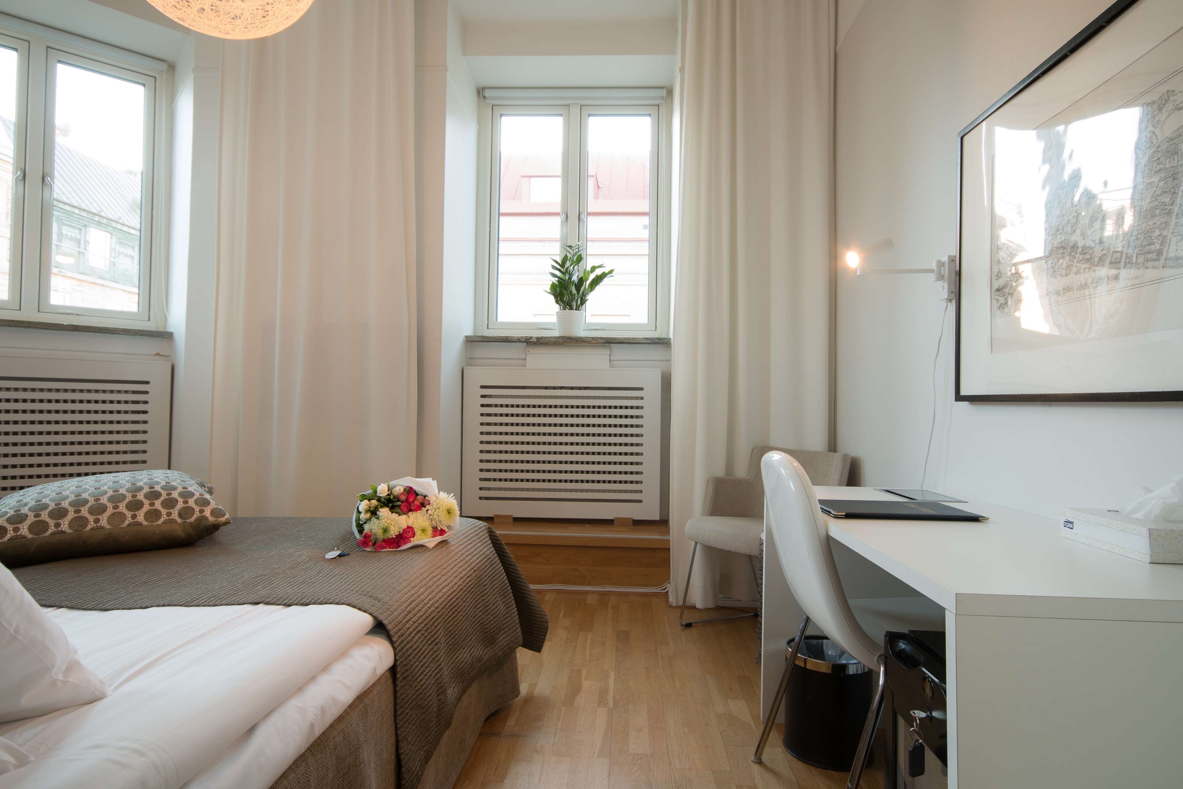 Et hotelværelse med en seng, et skrivebord, en stol, en radiator og et vindue med gardiner.