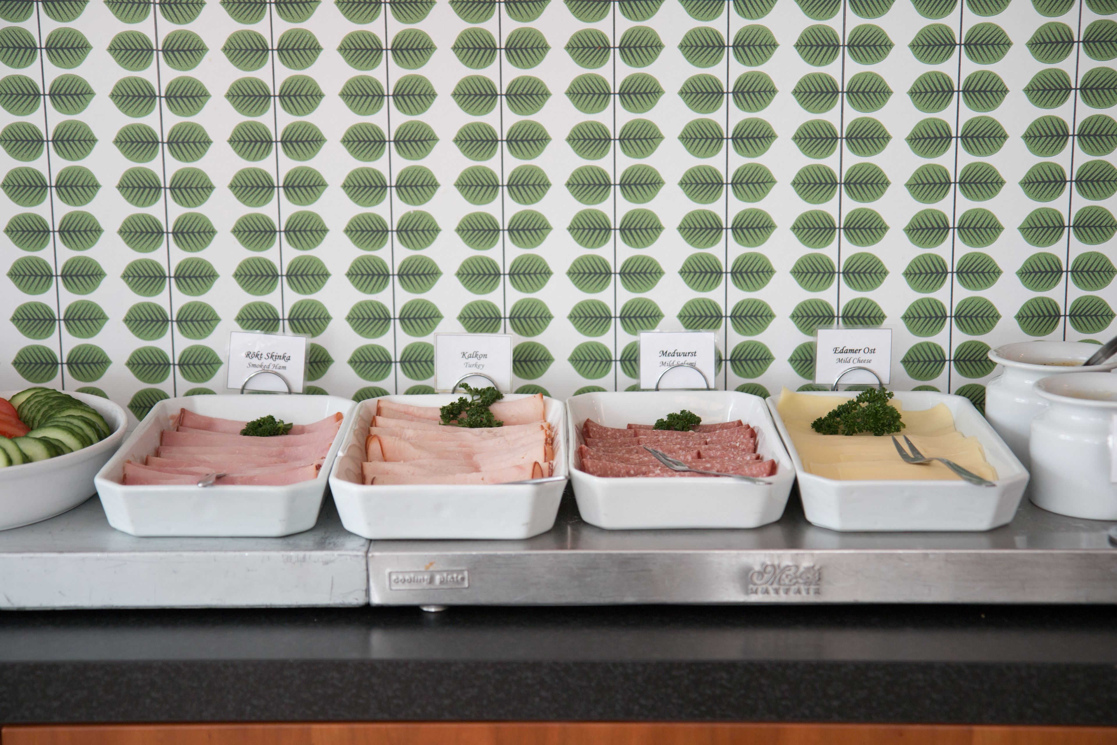 A buffet with various meat dishes labeled, including 'Smoked Ham', 'Kalkon Turkey', 'Medwurst', and 'Elamier Out'.
