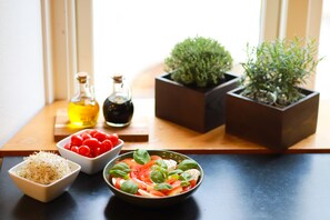 Una mesa con un tazón de ensalada, un tazón de tomates cherry, un tazón de queso rallado y dos botellas de aceite de oliva.