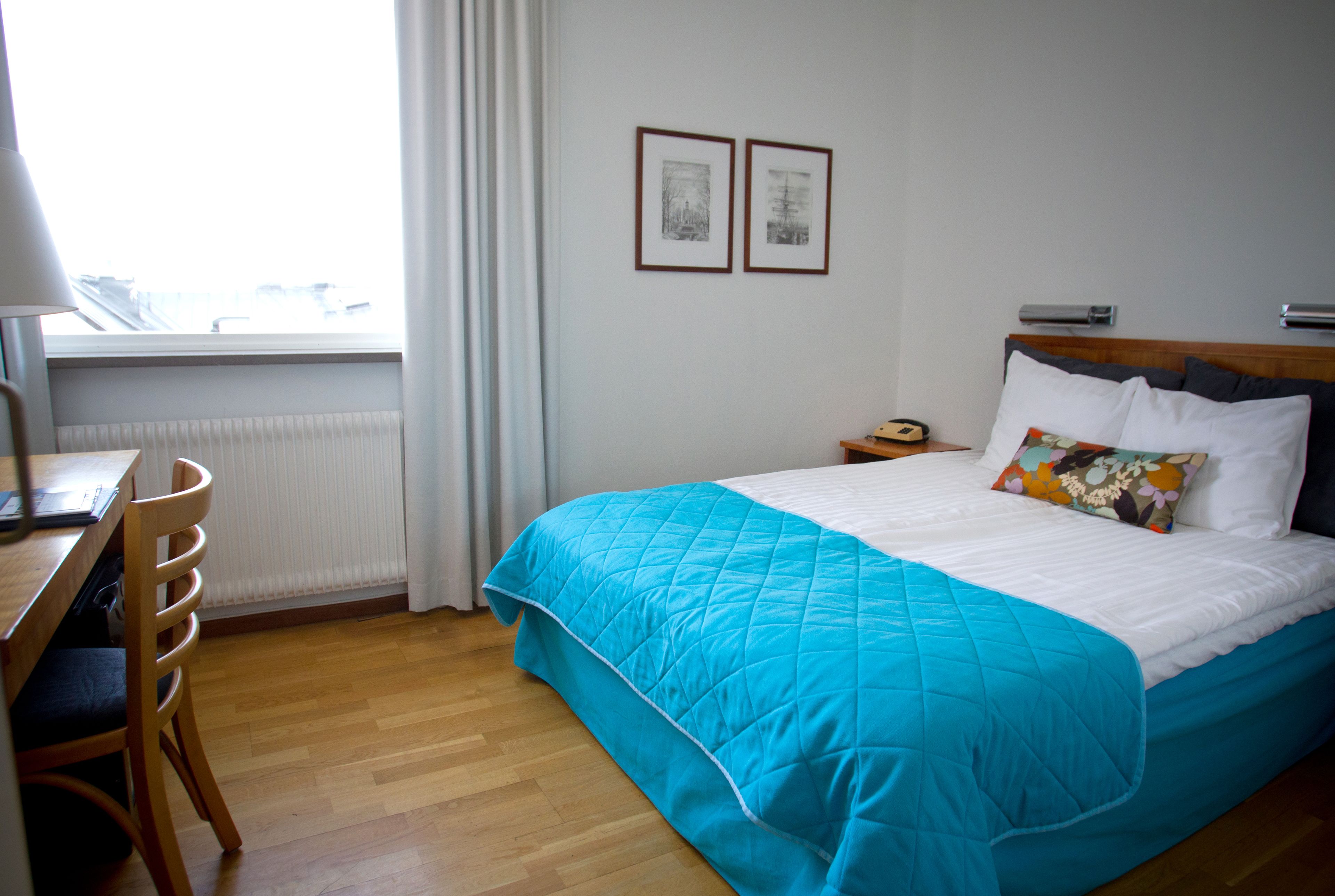 A hotel room with a bed, a desk, a chair, and a window with curtains.