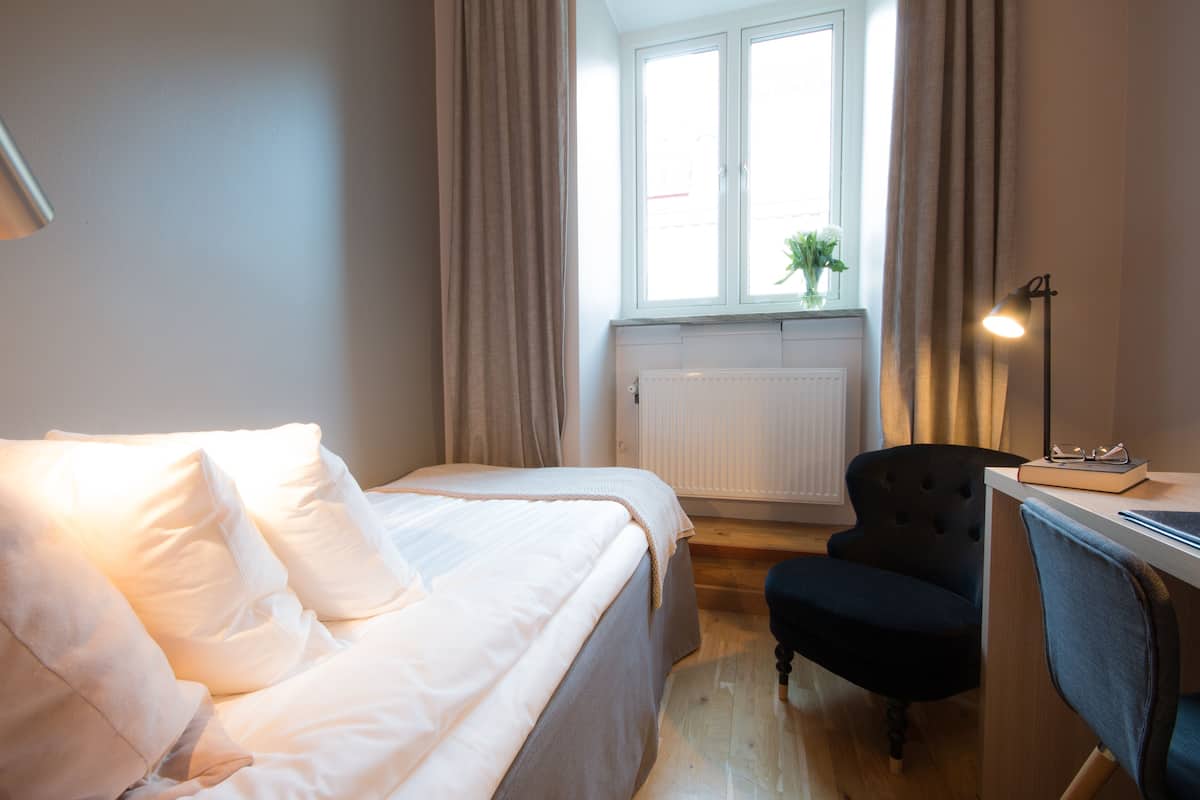 A hotel room with a bed, a desk, a chair, and a window with curtains.