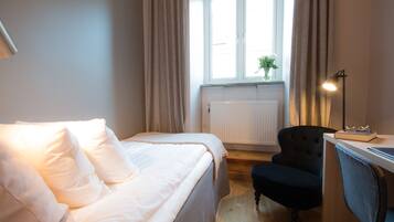 Et hotelværelse med en seng, et skrivebord, en stol og et vindue med gardiner.