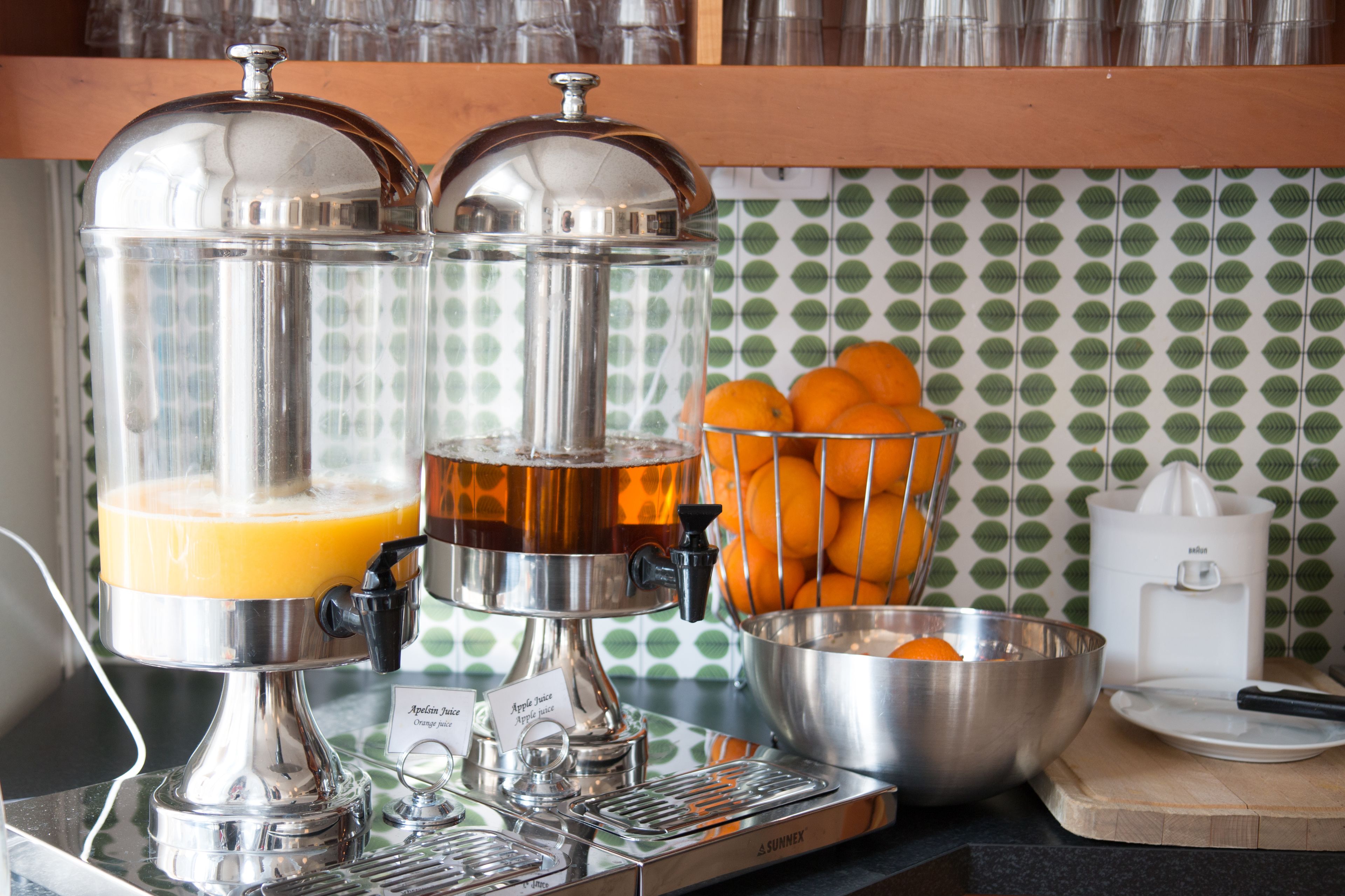 A kitchen with two fruit juicers, a bowl of oranges, and a juicer with a label.