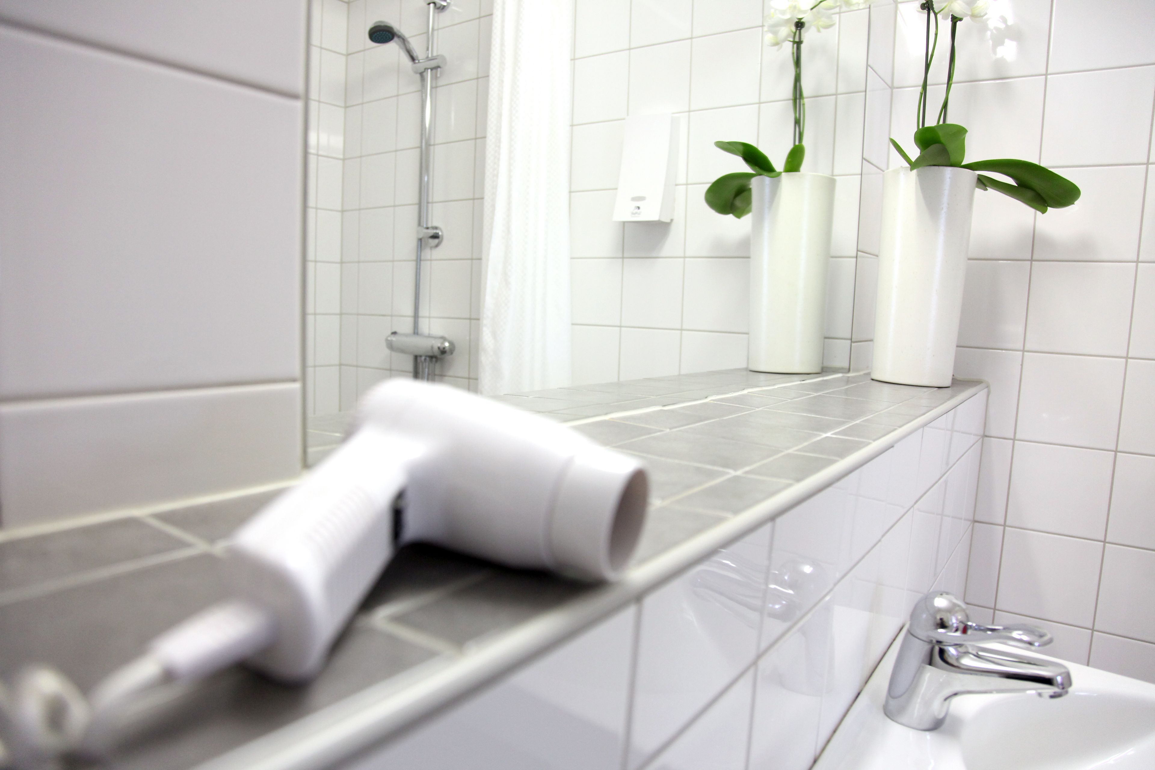 A bathroom with a shower, a sink, and two white vases with green plants on the counter.
