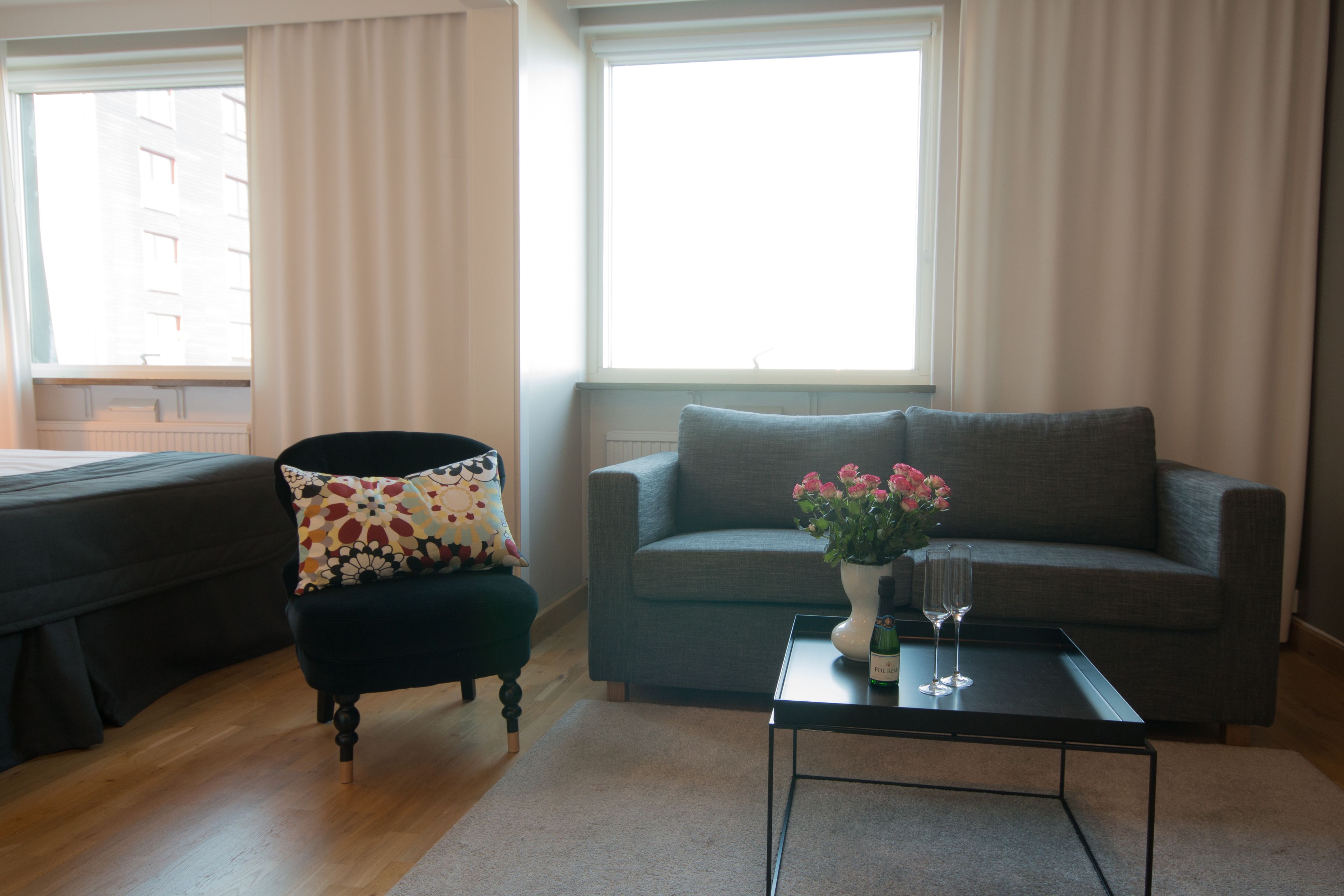 Una sala de estar moderna con un sillón oscuro, un sofá gris y una pequeña mesa de centro con un florero.