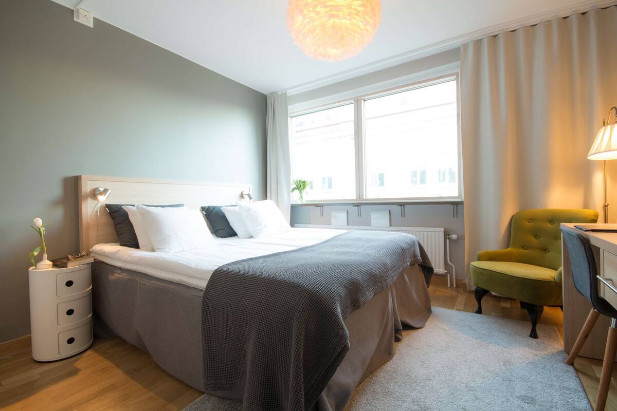 A bedroom with a bed, bedside table, lamp, chair, and window.
