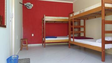 Quarto com duas beliches, um banquinho pequeno, um ventilador e uma cesta azul.