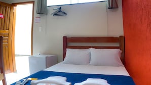 Habitación de hotel con cama, colcha azul, almohadas blancas y cabecera de madera. Hay toallas sobre la cama y un control remoto al lado.