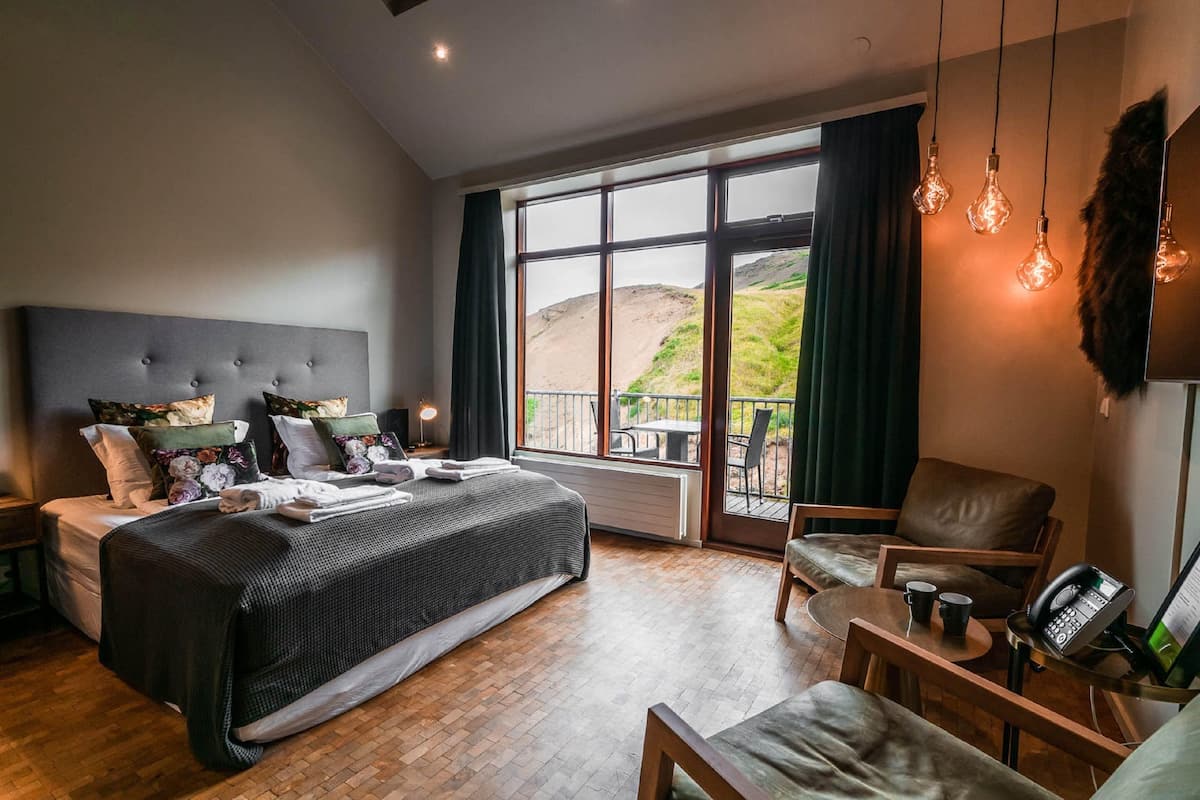 Un dormitorio amplio con una cama grande, una zona de estar con una silla y una mesa, y un balcón con vistas.