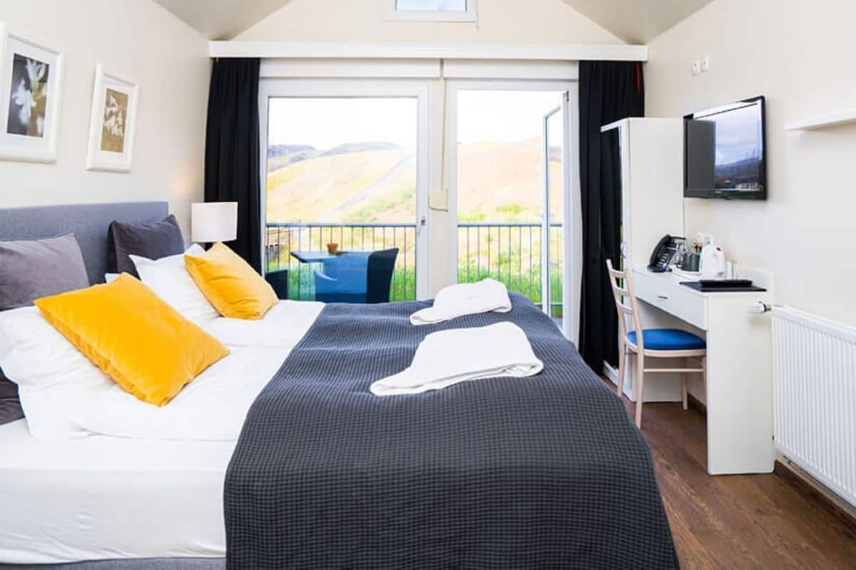 Habitación de hotel con cama, escritorio, silla, televisor y balcón con vistas.