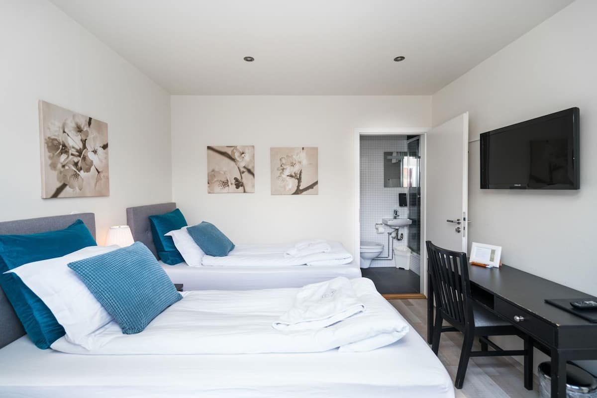 Habitación de hotel con dos camas, un escritorio, una silla, un televisor y un baño visible a través de una puerta abierta.