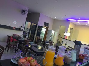 Un comedor de hotel con una mesa preparada para el desayuno, que incluye frutas y bebidas.