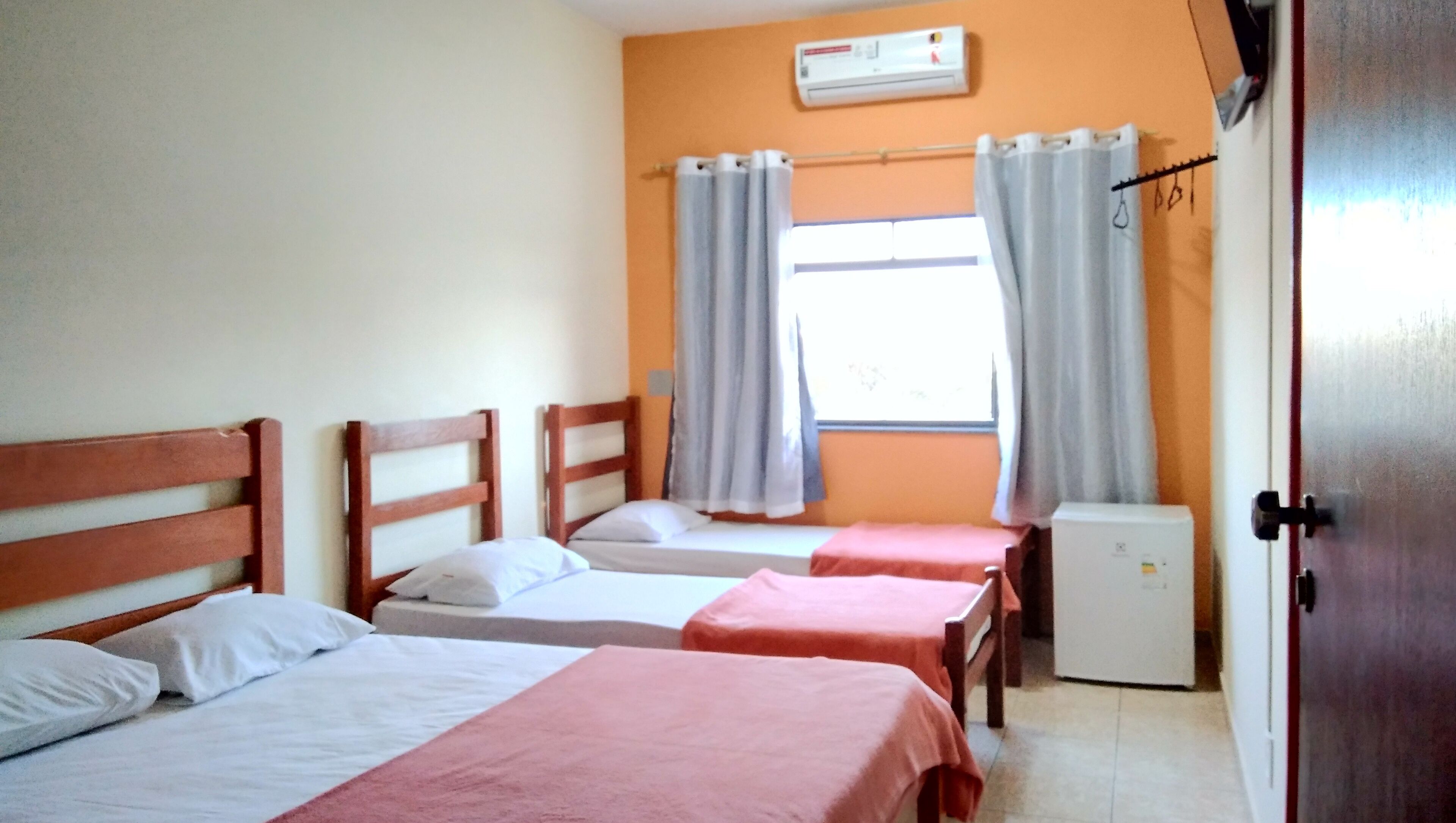 Una habitación con dos camas individuales, una mesita, una ventana con cortinas y una puerta.