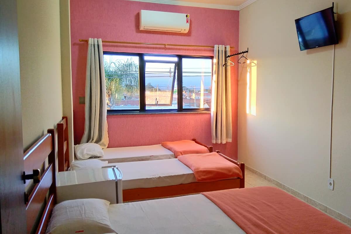 Una habitación con dos camas individuales, una ventana con cortinas, aire acondicionado, televisor y una puerta.