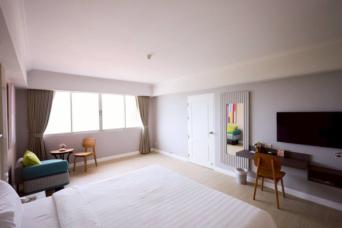 A hotel room with a large bed, a desk, a chair, a TV, and a window with curtains.