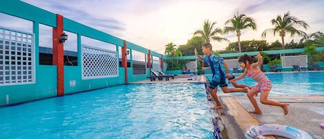 Une piscine aux couleurs turquoise et rouge, entourée de palmiers et de chaises longues.