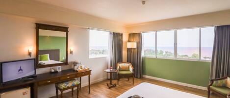 Habitación de hotel con cama, escritorio, silla, televisor y vista al mar.