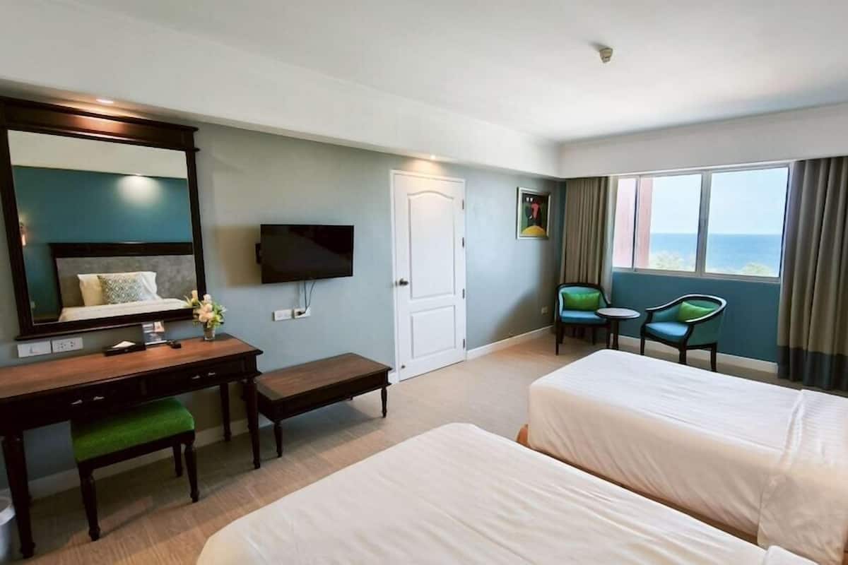 A hotel room with two beds, a desk, a chair, a TV, and a window with curtains.