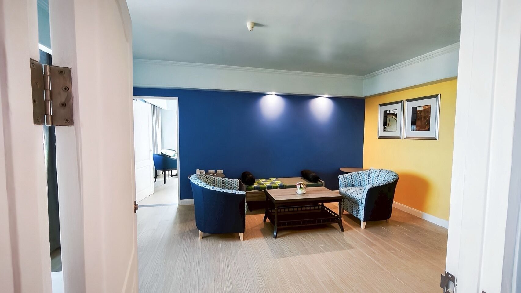 Une pièce avec un mur d’accent bleu, un plancher en bois, un canapé, un fauteuil à motifs et une petite table agrémentée d’un objet décoratif.