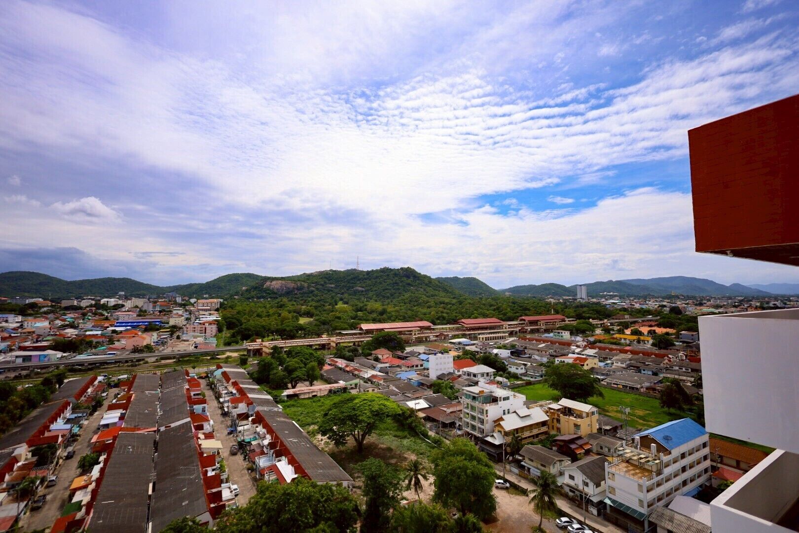 A cityscape with a mix of residential and commercial buildings, a prominent red-roofed structure, and a hilly backdrop.
