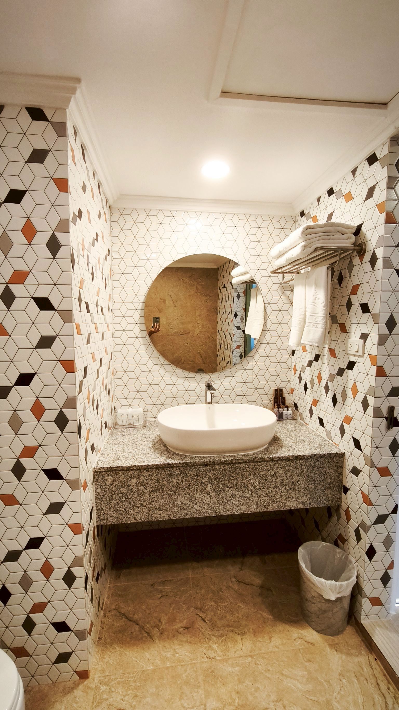 Un baño con espejo redondo, lavamanos blanco y paredes de azulejos con diseños geométricos.