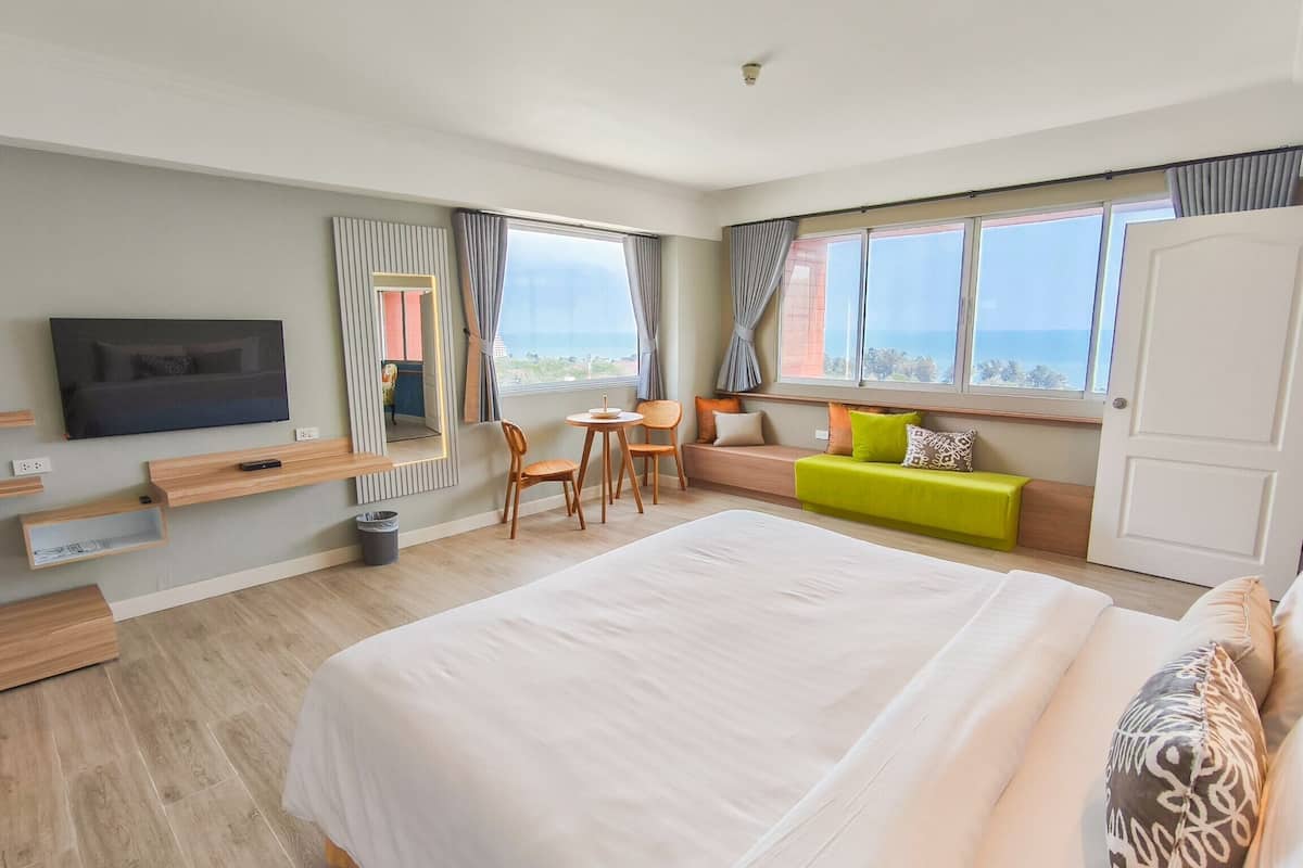 A modern hotel room with a large bed, a TV, a seating area with a view, and a small table.