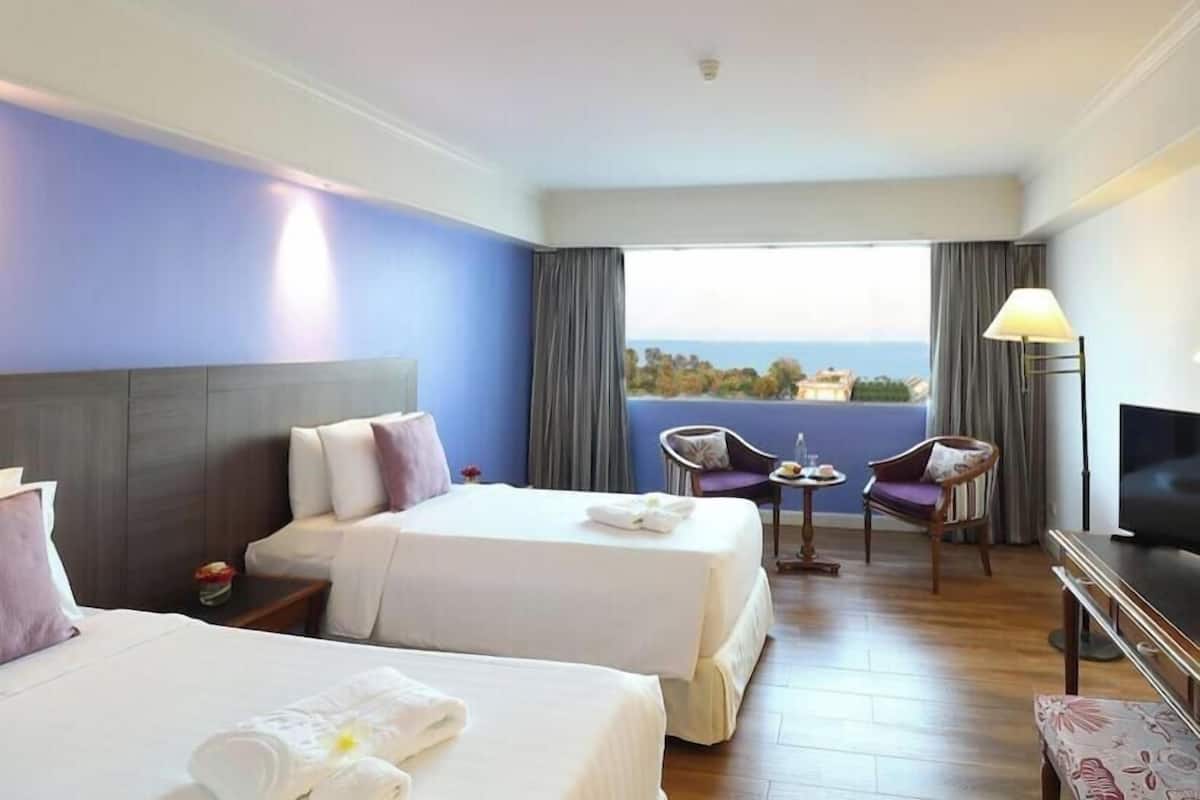A hotel room with two beds, a TV, a balcony with a view, and a table with chairs.