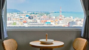 A room with a view of a cityscape, a round table with a bowl, and two wicker chairs. - HUA HIN GRAND HOTEL AND PLAZA (Hua Hin)
