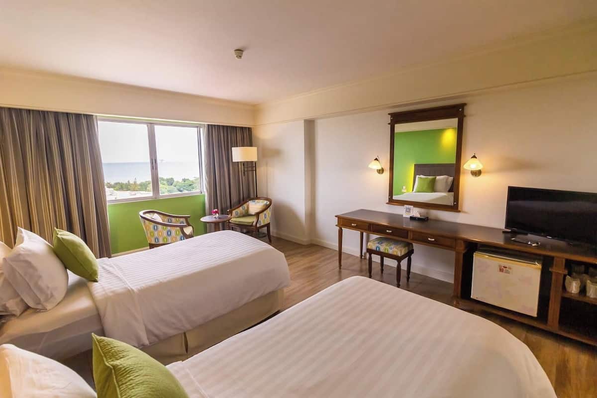 A hotel room with two beds, a desk, a television, and a view of the outdoors.
