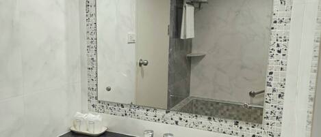 Un baño con un lavabo blanco, un espejo grande y una zona de ducha.