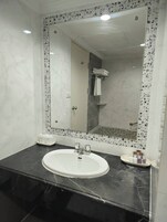 Un baño con un lavabo blanco, un espejo grande y una zona de ducha.