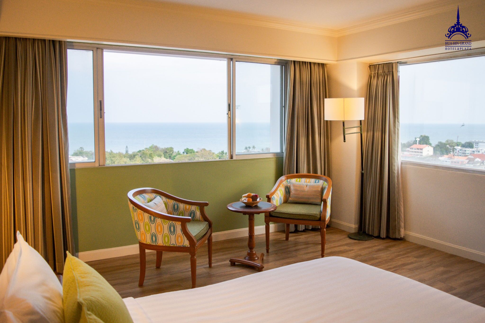 A hotel room with a large bed, two armchairs, a small table, and a view of the sea.