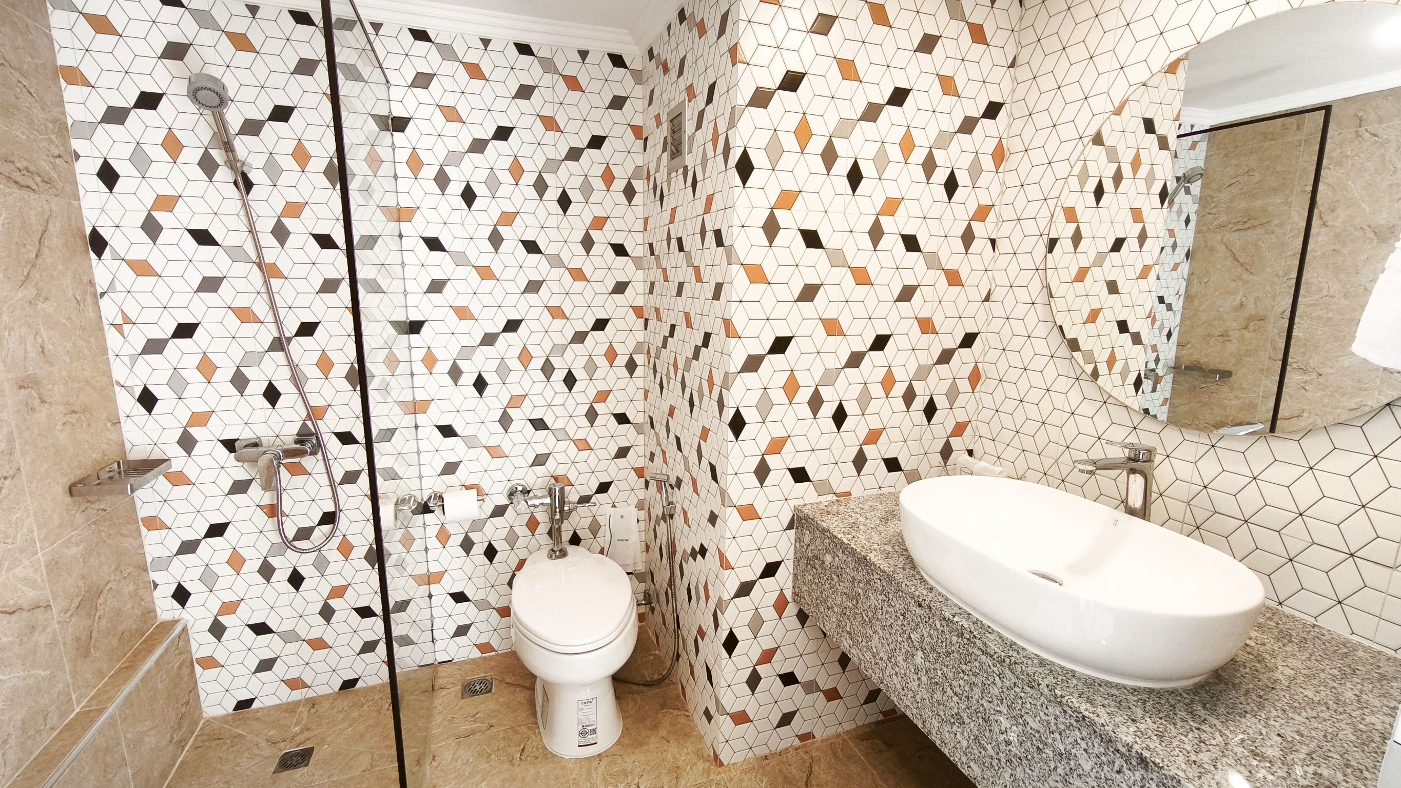 A bathroom with a geometric tile pattern, a toilet, a sink, and a shower.