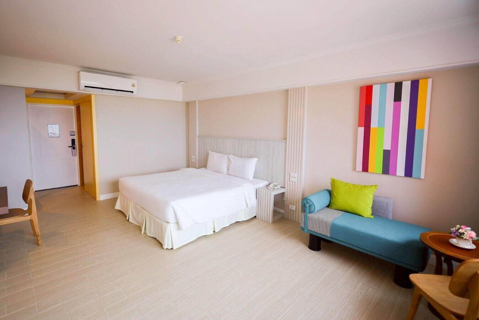 A hotel room with a large bed, a small sofa, a desk with a phone, and a colorful abstract painting on the wall.