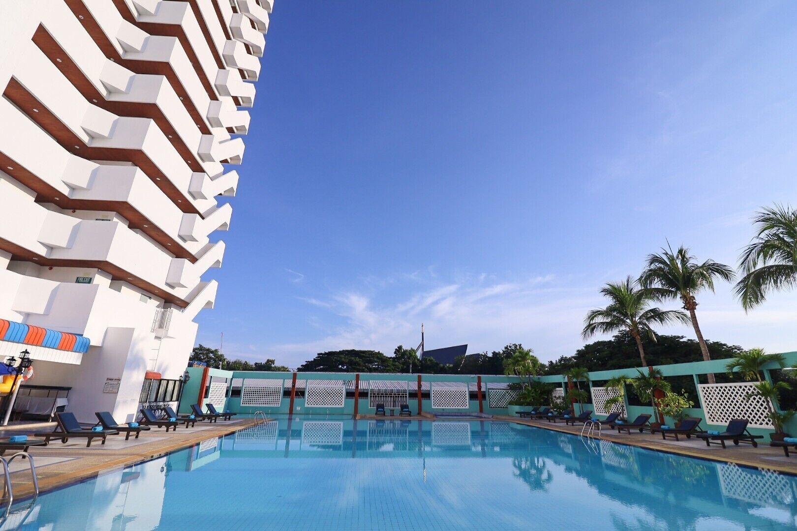 Une piscine avec des chaises longues, un ciel bleu azur et des palmiers.