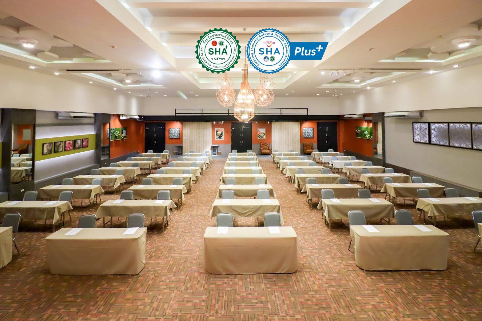 Une salle de conférence avec des rangées de tables et de chaises, une moquette à motifs et un lustre.
