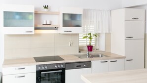 Una cocina moderna con armarios blancos, horno integrado, lavavajillas y una ventana con una planta.