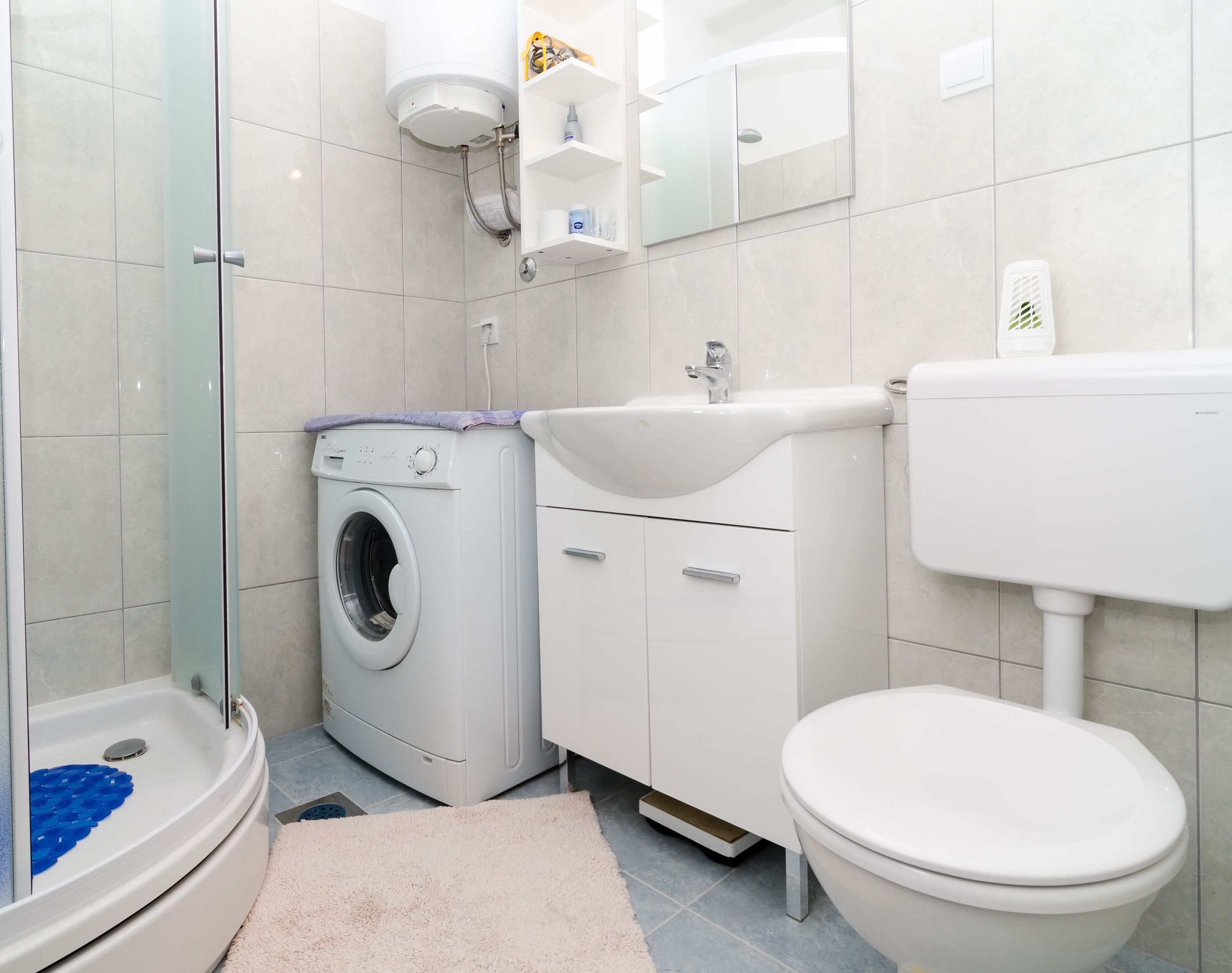 A modern bathroom with a washing machine, sink, toilet, and glass shower enclosure.