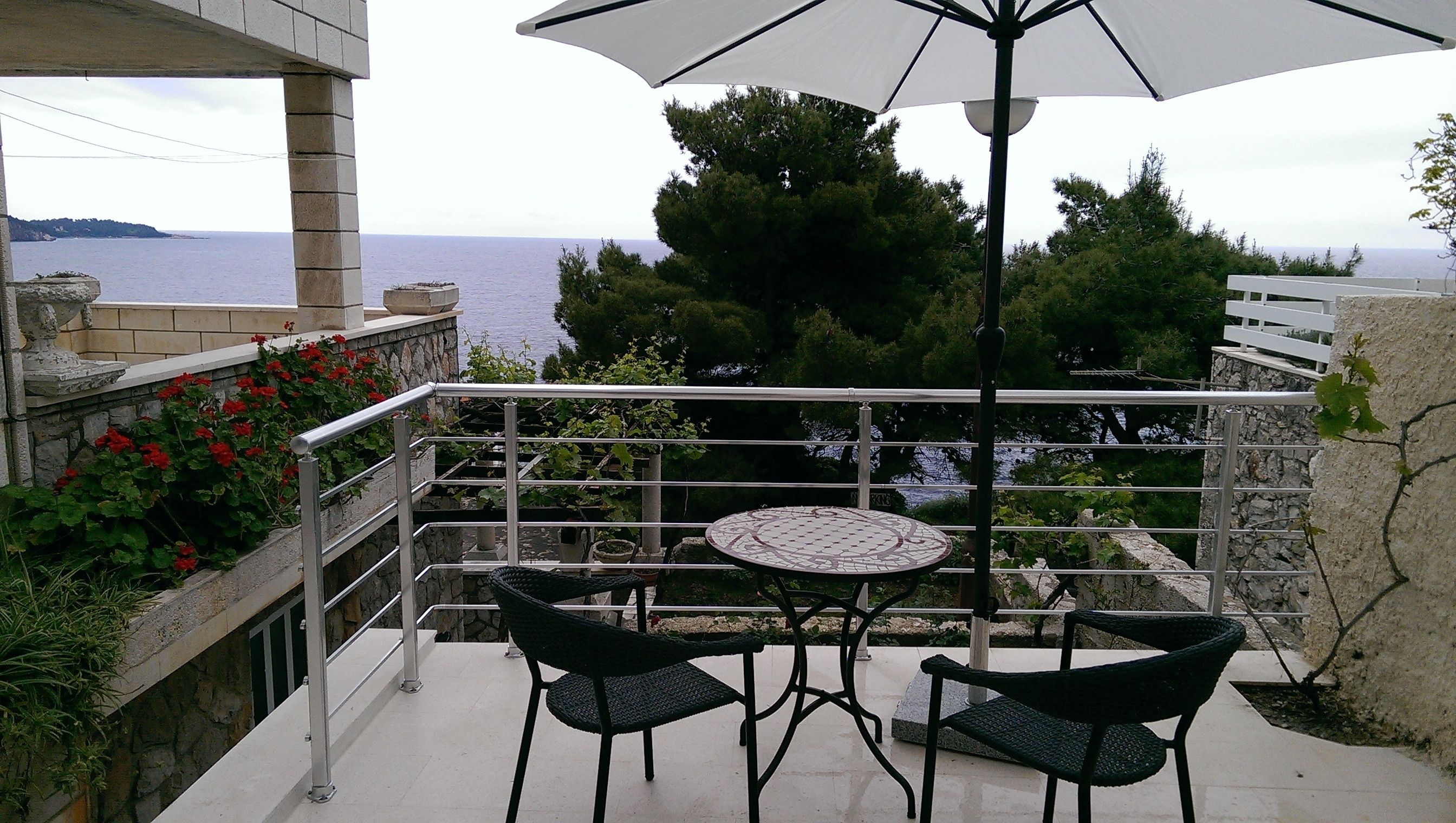 Un balcon avec une table et des chaises, un parasol blanc et une vue sur la mer.