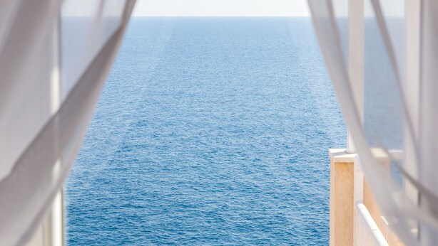Vista a través de una ventana con cortinas translúcidas, mostrando un cuerpo de agua y un cielo despejado.