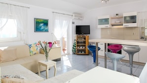 Una sala de estar moderna con un sofá, una mesa de centro y un televisor. Cuenta con una cocina con mostrador y taburetes.